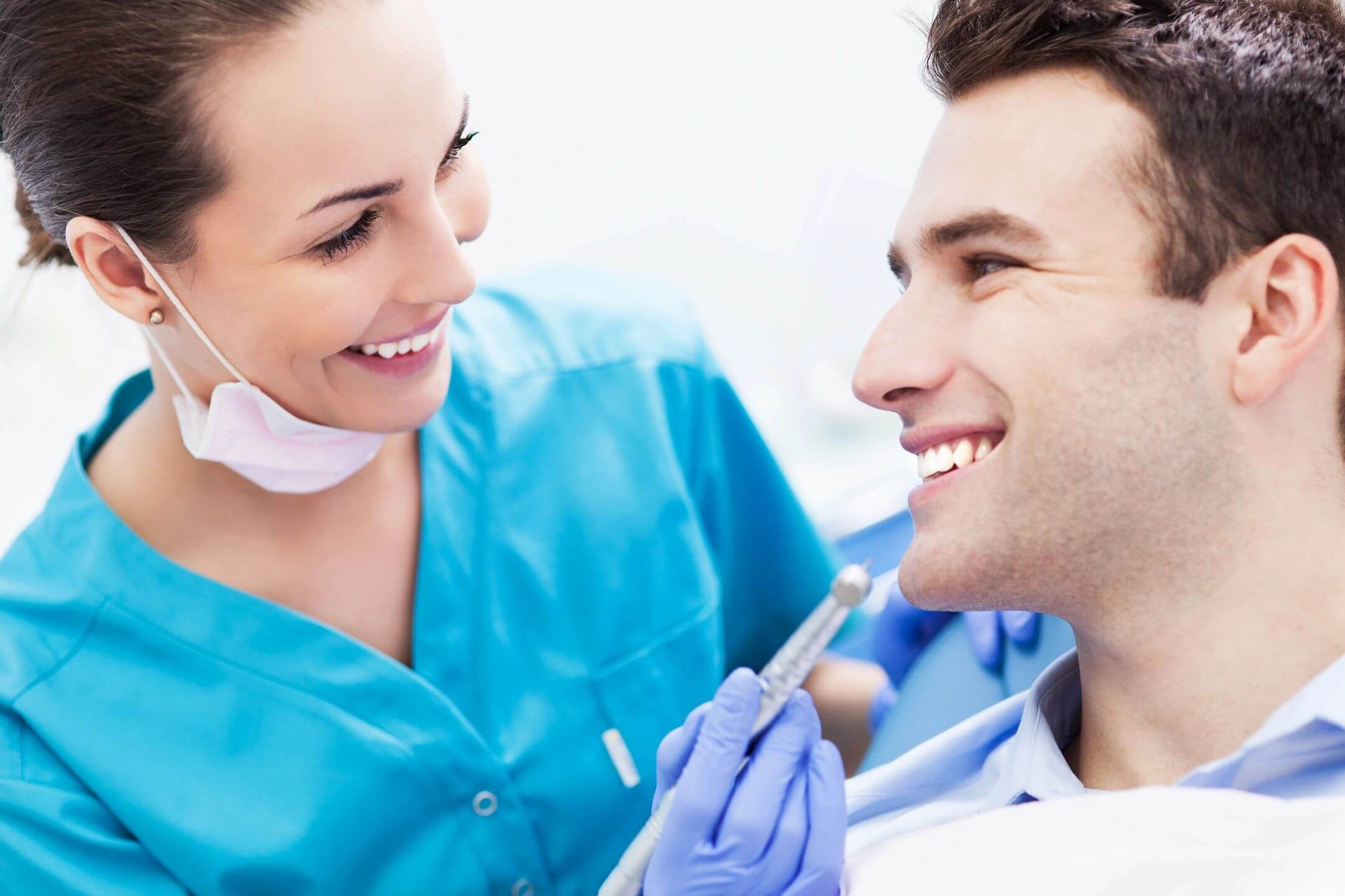 Dentist smiling while examining a male patient's teeth.